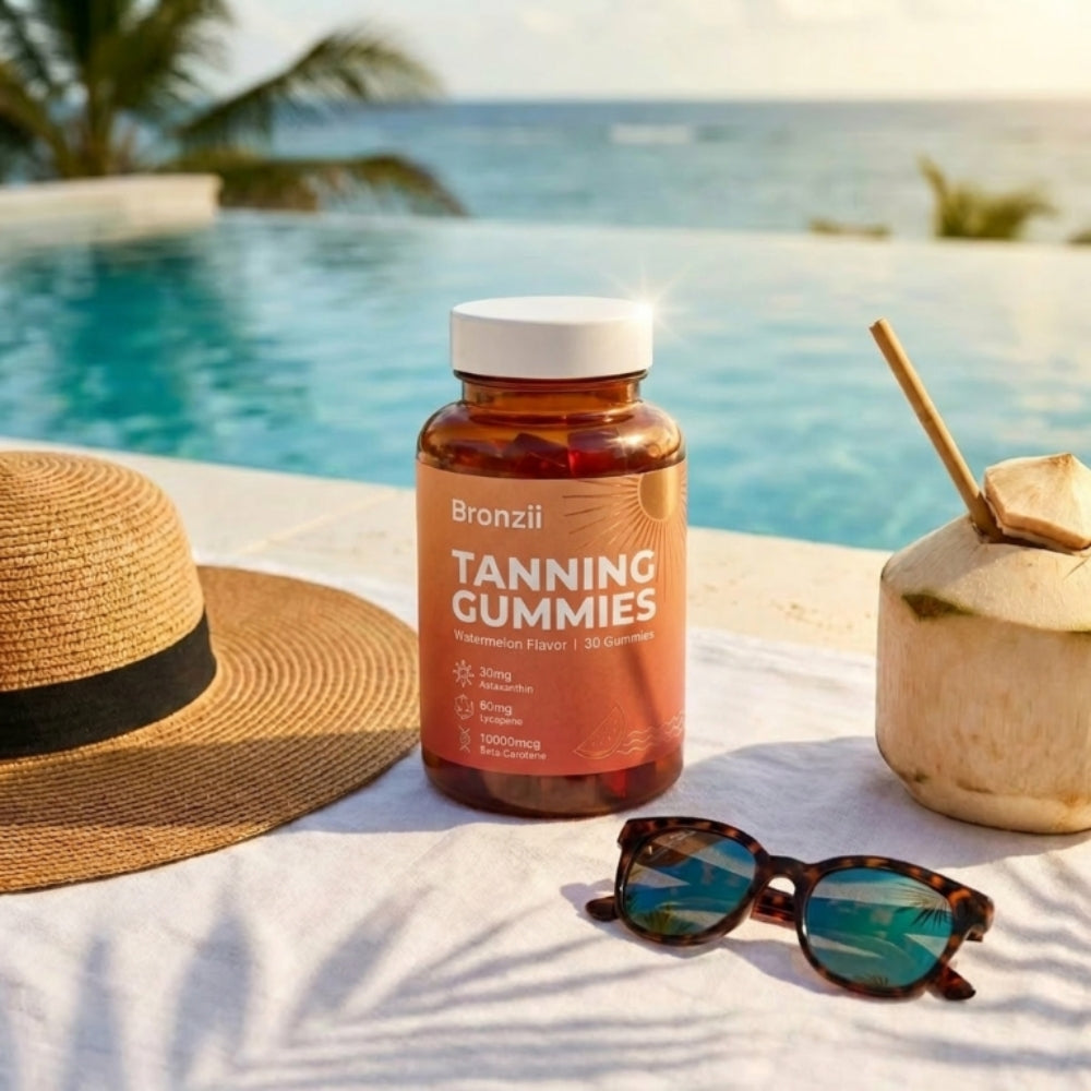 A bottle of tanning gummies on a towel by a pool with a hat, sunglasses, and a coconut.